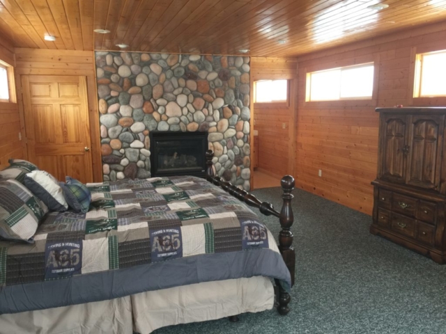 Third floor master bedroom with fireplace and private bathroom, including shower at Torch Lake Lodge. Bedroom includes private deck overlooking trees and fire pit.